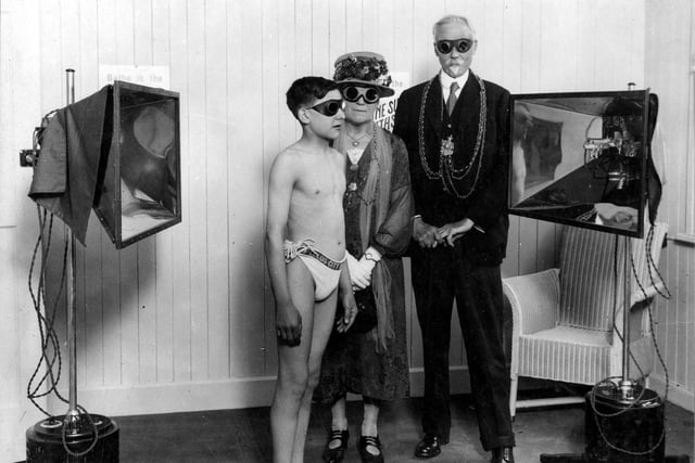 A young boy demonstrates the benefit of the Alpine Sun Baths at the City Baths on Cookridge Street in July 1927. These were designed by Cuthbert Brodrick and also known as the Oriental and General baths. The boy wears regulation Leeds City Baths bathing trunks and protective eye goggles. These goggles are also worn by the Lord and Lady Mayoress, Alderman Hugh Lupton and his wife. Ella to protect their eyes from the reflective rays of the two enormous sun lamps. theraputic sunbathing or 'Sun cure' was a widely prescribed medical treatment for such diverse conditions as rickets, tuberculosis, cholera, viral pneumonia, bronchial asthma, gout, jaundice and severe wounds.