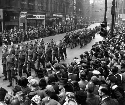 Military parade on Boar Lane, which was part of the route taken which ended at Leeds Town Hall on The Headrow. Unseasonably bad weather had delayed the Normandy Invasion Forces, the D-Day landings took place 3 days later on the 6th of June. Many of the people seen here in the crowd are wearing coats and hats, prepared for rain.