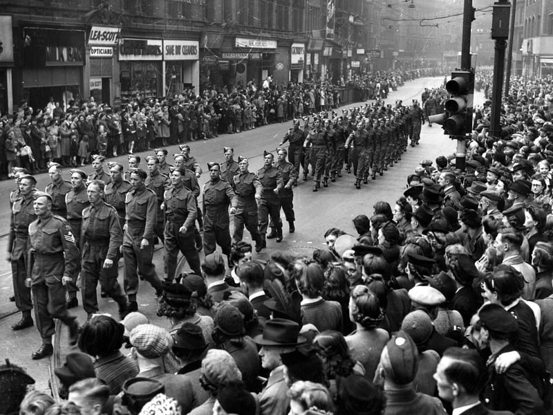 Military parade on Boar Lane, which was part of the route taken which ended at Leeds Town Hall on The Headrow. Unseasonably bad weather had delayed the Normandy Invasion Forces, the D-Day landings took place 3 days later on the 6th of June. Many of the people seen here in the crowd are wearing coats and hats, prepared for rain.