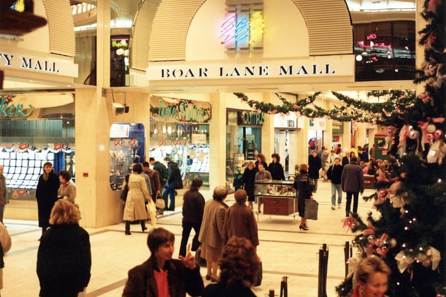 Leeds Shopping Plaza showing Boar Lane Mall, busy with shoppers around Christmas time, with decorations and a Christmas tree visible. This shopping centre was formerly the Bond Street Centre and opened in September 1977; in March 1996 it became the Leeds Shopping Plaza under new owners Tops Estates. Shops in the picture include James Walker, Olympus and Ibiza.