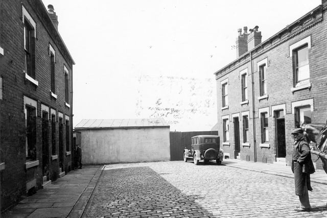 Clark Mount showing cobbled street with rows of terraced houses to each side. A workman with a horse in the middle of the street. A car is parked in front of gates that belong to Yorkshire Plasterers Ltd. Pictured in June 1935.