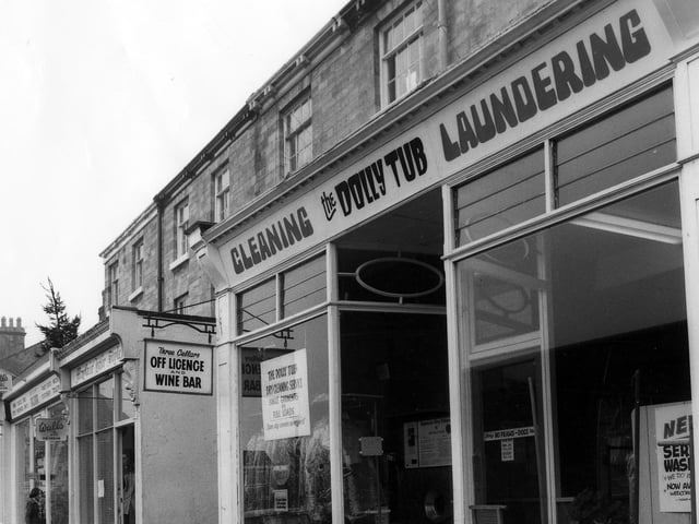 A row of shops on Boston Spa High Street pictured in March 1979. In the foreground is the Dolly Tub Launderette, with the entrance to the Three Cellars off licence and wine bar to the left. Next to this is Mayfair Hair Studio, then a shop selling fancy goods, stationery and ice cream. On the end of the row is the Spice Box restaurant.