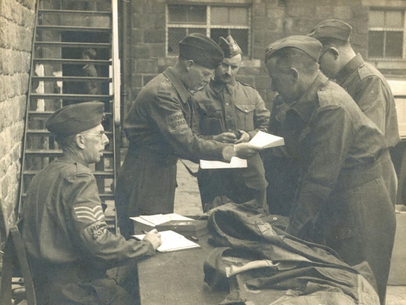 This photograph, circa 1940, is entitled 'Issue of uniforms at East Moor School, Autumn 1940'. East Moor Approved School for Boys was in Adel. Built in 1857, it became an Approved School in 1933 and finally closed in 1991. Major Oldendorff was Superintendent of East Moor School at this time. Denim overalls were initially issued, then replaced with standard battledress as being issued in this photograph by the end of 1940 due to supply issues.