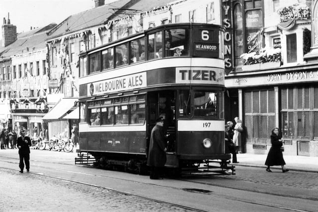 Shops decorated on Lower Briggate to celebrate the coronation.  These include Weaver to Wearer tailors and Gaskell & Chambers Ltd., bar fitters, on the left and John Dyson & Sons Ltd., clockmaker and jeweller, on the right. Tram no.197, a 'Horsfield' built 1930-31, is pictured on route 6 to Meanwood.