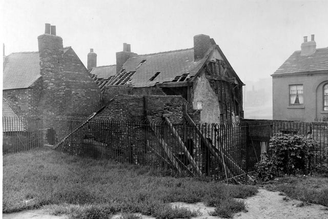 The back of an ancient and derelict building in Mabgate pictured in September 1919. The wooden frame of the building can clearly be seen with old brickwork beneath. The building, which could have dated from the medieval period, was due to be demolished. Iron railings surround the property, and grass and bushes can be seen in the foreground.
