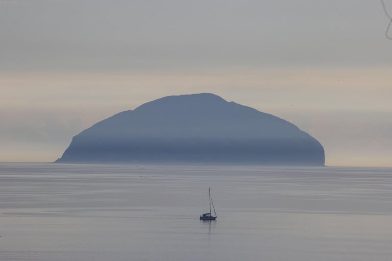 A lone boat sails across clear, settled waters near Ailsa Craig