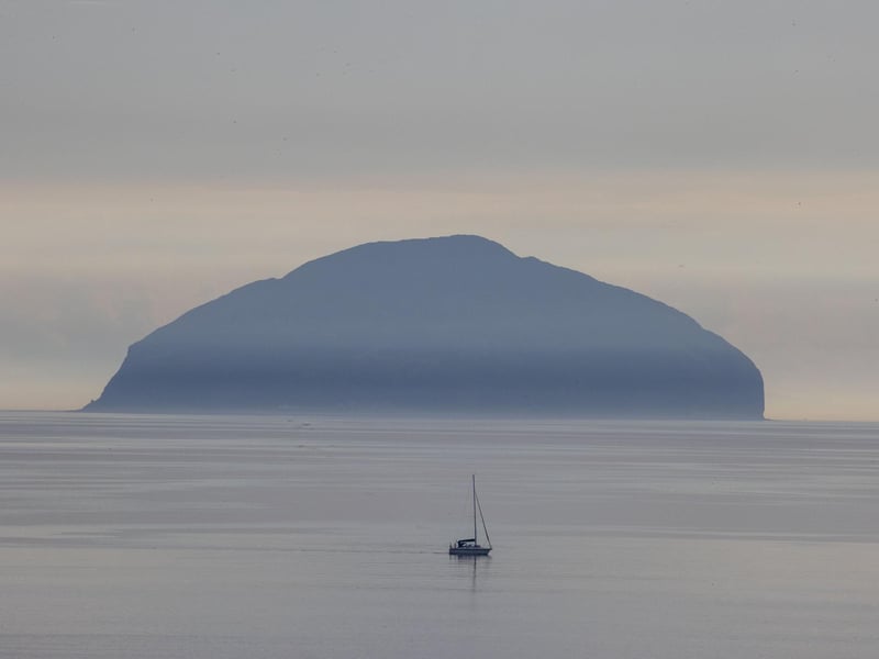 A lone boat sails across clear, settled waters near Ailsa Craig