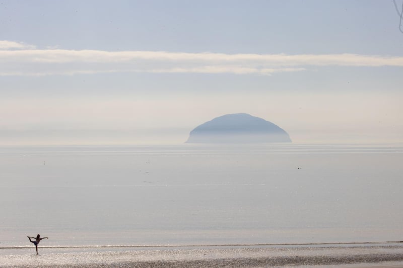 A woman stretches in the shallow waters of the Ayrshire Coast as the sun shines on Ailsa Craig