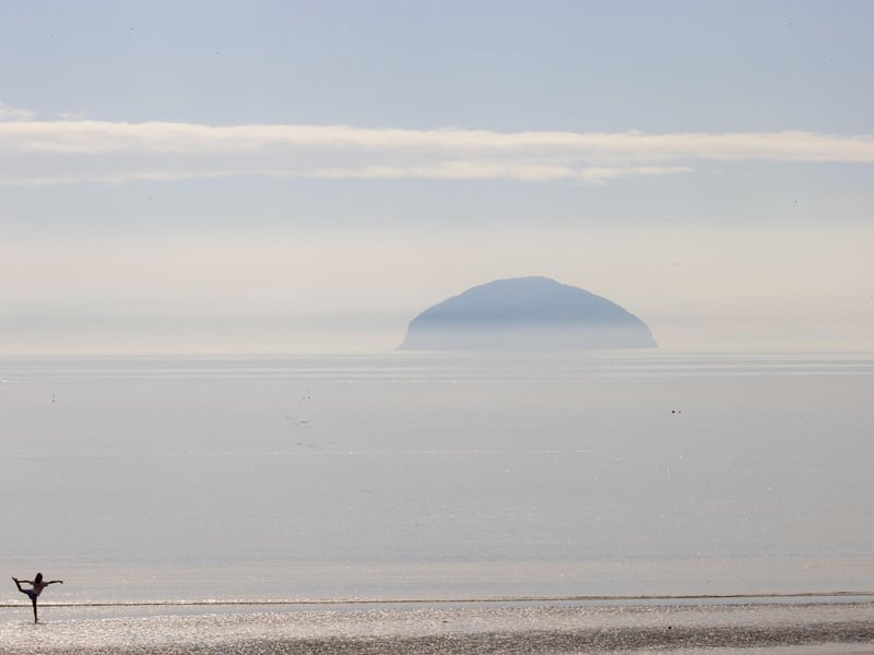 A woman stretches in the shallow waters of the Ayrshire Coast as the sun shines on Ailsa Craig