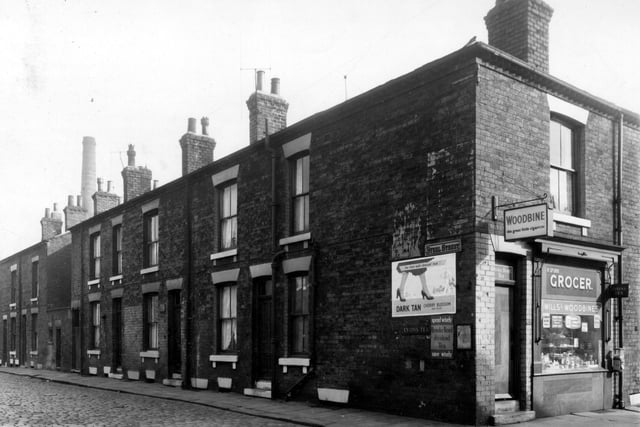 Steel Street runs from the left edge of this view, numbers run in descending order to number 2 on the right. On the right edge is a grocers at number 27 Orchard Street business of R. Spurr. An advertising sign polish is visible as well as a hanging sign for 'Woodbine the great little cigarette'. Pictured in September 1958.