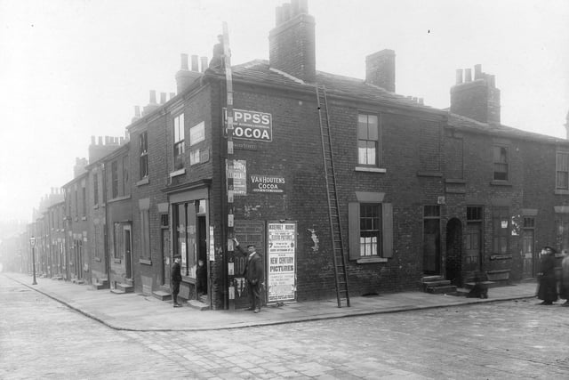 The corner of Edward Street and Templar Street, showing derelict houses. Two workmen are holding a measuring pole against wall of the corner shop. Two small boys standing outside entrance to Bakehouse Court can be seen to the right. Poster for Assembly Rooms, Briggate. Pictured in October 1910.