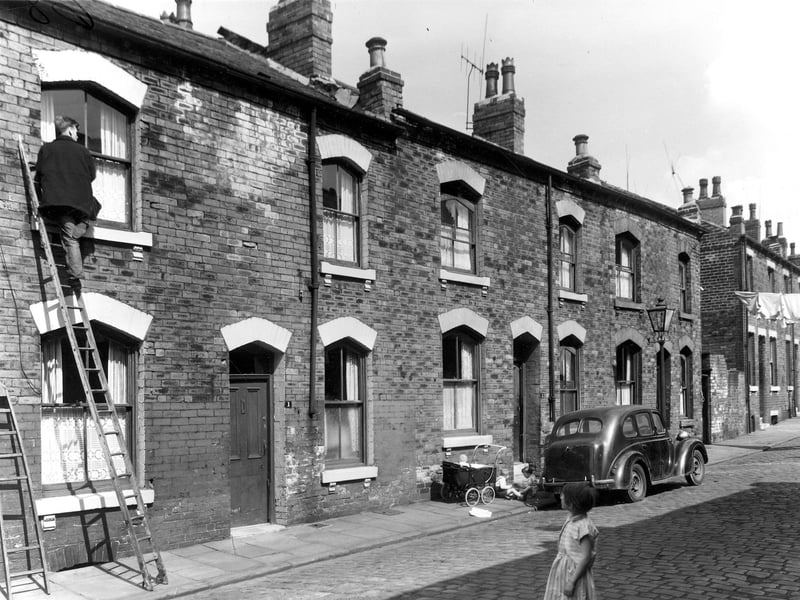 A window cleaner is at work on a bedroom window on Perth Street in May 1960. To the right children play outside.