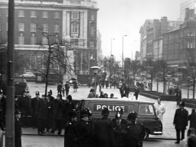 Policemen in uniform, assembled near the Garden of Rest and War Memorial on The Headrow. A police van is also parked in Calverley Street.