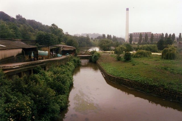 A view from the direction of Armley Mills towards Kirkstall Power Station, seen right. The Power Station was built between 1928 and 1930 by the City of Leeds and further extended between 1943 and 1944. It closed in October 1978 and the cooling towers were demolished in 1979. The remaining buildings were cleared by 1986. In the centre the weir is visible on the River Aire. To the left there are a series of ramshackle buildings between the canal and the river (the Leeds & Liverpool Canal is behind the buildings, left). A couple of vardos or Romany caravans can be seen. The trees on the left are part of Cunliff Wood.