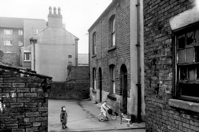 Two boys play in the yard, the one to the right rides a tricycle and has a cowboy hat in his hand on Moorville Place in April 1959. On the left edge of this view in the background part of Shaftesbury House can be seen which was, until recently, used as a hostel.