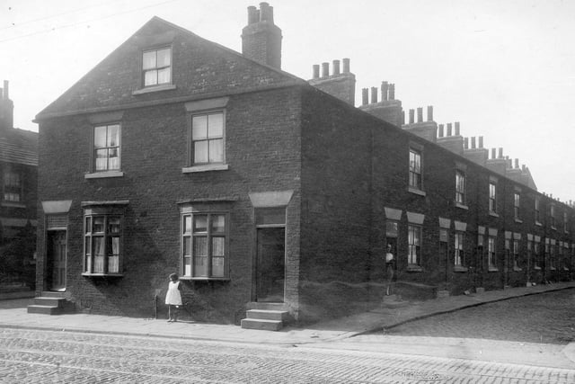 A little girl stands on Low Road outside number 40 which is the property of Samuel Mulholland at 42 lived James Richardson, grinder. View of Latimer Street shows a row of back-to-back terraced houses. A woman stands in doorway of first house.