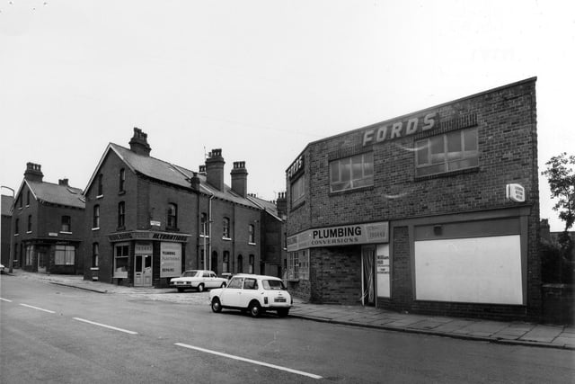 Burley Road showing the junction with Cross Greenhow Avenue in the centre in July 1975. To the right of the junction is the business of T. & L. Ford, builders, plumbers and joiners. On the corner at the far side of Cross Greenhow Avenue is another building with the Ford name on it, possibly vacated as they moved to larger premises. Further to the left are junctions with Cross Greenhow Place and Cross Greenhow Street. Houses on these streets have since been demolished and replaced by new houses on Greenhow Gardens, but the Ford's building on the right survives, now named Thomas House and in 2022 was occupied by Angel's Hair & Beauty Salon.