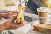 Woman eating a breakfast sandwich and drinking coffee while working with a laptop