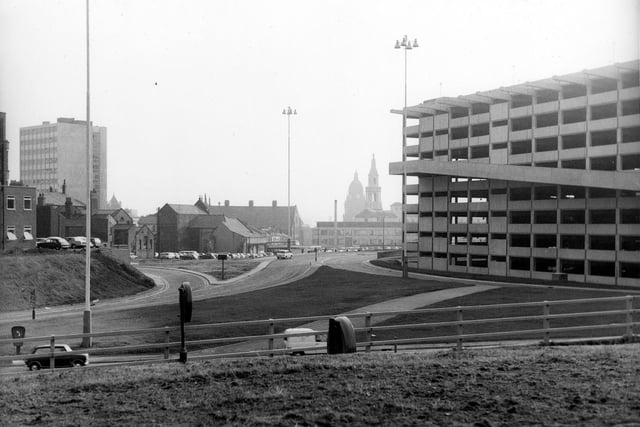 The Leeds Inner Ring Road as it joins Woodhouse Lane. Visible in the distance are the clock tower of the Town Hall and one of the gilded owl topped twin pinnacles of the Civic Hall. On the right is the Woodhouse Lane car park, opened August 6, 1970 with 1,100 spaces.