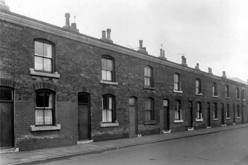 A long view of terraces housing on Clarence Road. Houses have sash windows, the lower halves of which are curtained with white nets customary at the time.
