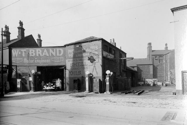 A view of W. T. Brand, Motor Engineer on Chapeltown Road, showing garage premises with petrol pumps to rear and side. Visible on the right is the edge of the Cambridge Hotel public house while buildings in the background between the two face onto St. Clement's Place. Pictured in April 1937.