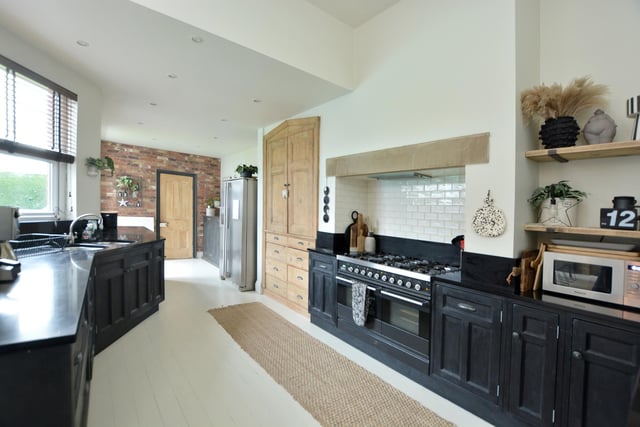 An open rectangular archway leads to the kitchen area, which has a well-designed layout of low level painted base units and drawers with granite worktop surfaces and splashbacks, and has space for a range style cooker set within the original chimney breast, with decorative stone lintel and overhead filter hood.
