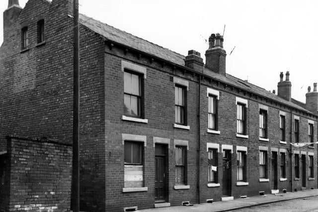 Four double fronted back-to-back terraced houses on Falmouth Place  in July 1965. They are flanked by yards originally built to house the shared outside toilets. Clothes hang on washing lines stretched across the street and number 17 on the left has a boarded up window.
