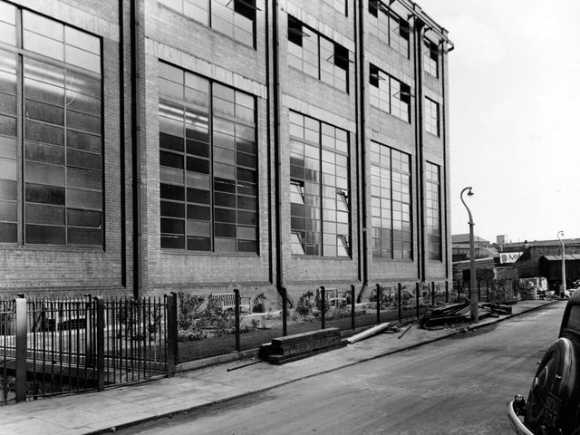 R. W. Crabtree and sons printing machine manufacturing in August 1955. Photo is of close up of windows on long side of building. Windows in metal frame have 44 panes of glass. Wooden benches and small formal garden run along one side.