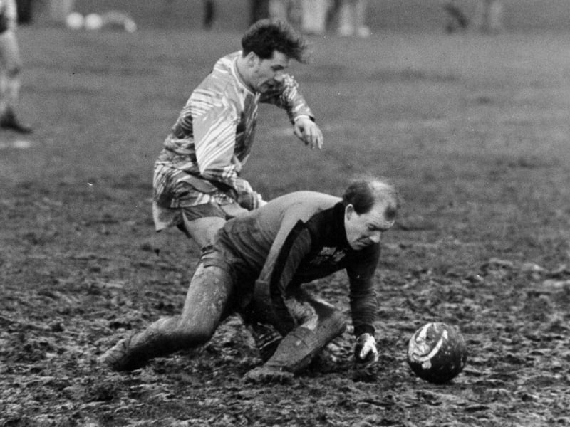 Dirty play. Crown Reserves goalkeeper Craig Eustace scrambles for the ball on a mud bath Stray pitch under pressure from CEGB striker Michael Oakes. Pictured in February 1990.