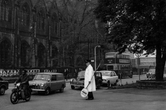 Leeds Grammar School in June 1967. The traffic on the road in front includes a mini van, motor cycle and a bus. A lollipop man is in the foreground.