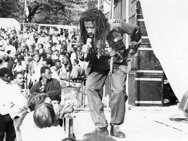 Jamaican Dub poet, Ras Fikre, performs to the crowds at the 4th annual Black Music Festival on Bank Holiday Sunday, August 1989. It was a free community event sponsored by Leeds City Council and was the biggest Black Music Festival in Europe. It was held annually in Potternewton Park and included musicians and performers from the Caribbean and the USA. As well as the more well known artists, the Festival also provided a showcase for local talent.