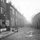 Black Swan Yard in Leeds city centre pictured in October 1898. Part of North Street Improvement Area, was number 2 North Street, now part of Vicar Lane. On the left houses, some with basements, access down steps from pavement. Railings act as barriers to open area. There are two wall signs for T. Butter, Coach builder. At the end of the yard are outside toilets and a cart. To the right, premises with wooden steps to upper doors. Yard has some cobbles, other parts unsurfaced.