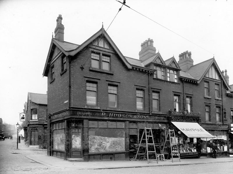 A parade of shops on corner of Malvern Road and Beeston Road in May 1936. To left can be seen The Harrisons Arms, with Tetley sign outside, also a street lamp, letter box and cars. End of Brookdale Place is also in view. Shops in main view are, from left to right, R. Hudson and Sons, drapers; Maypole Dairies and another unidentified shop. In front of R. Hudsons are two large ladders with a plank between them.