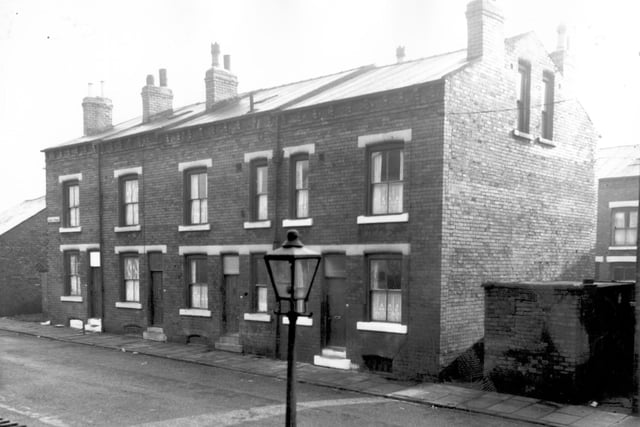 Two double fronted and two single fronted back-to-back terraced houses on Ascot Street flanked by yards originally built to house the shared outside toilet and midden. 58 is on the right through to 64 on the left. The arches at pavement level show where the basement windows were before road improvements raised the height of the street and filled them in. Pictured in October 1966.