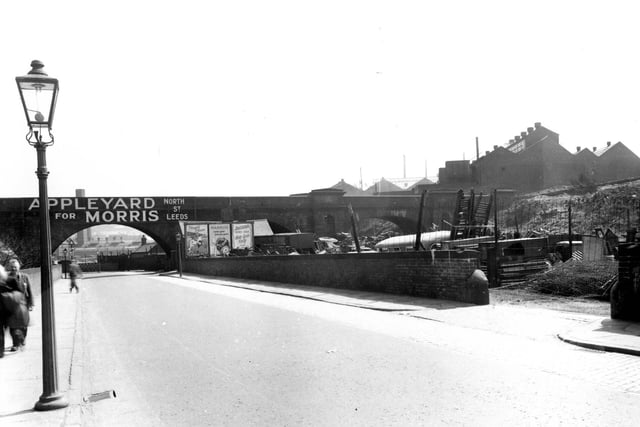 Viaduct Road which passes under the L.N.E.R railway track pictured in May 1956. The premises of 'Appleyard for Morris, on North Street', is advertised across the bridge. To the right is 'Appleyards Scrapyard', with ladders, fencing, crates and an old bus visible behind the wall. Houses can be seen alongside factories in the top right of the photo.
