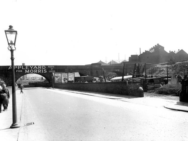 Viaduct Road which passes under the L.N.E.R railway track pictured in May 1956. The premises of 'Appleyard for Morris, on North Street', is advertised across the bridge. To the right is 'Appleyards Scrapyard', with ladders, fencing, crates and an old bus visible behind the wall. Houses can be seen alongside factories in the top right of the photo.