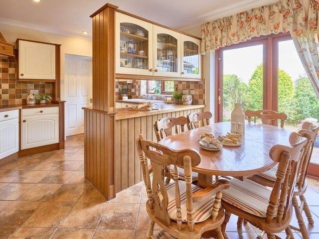 A peninsula work unit divides the dining and preparation area, which features a range of farmhouse style cream cabinetry finished with solid wooden worktops and a traditional sink beneath the window.