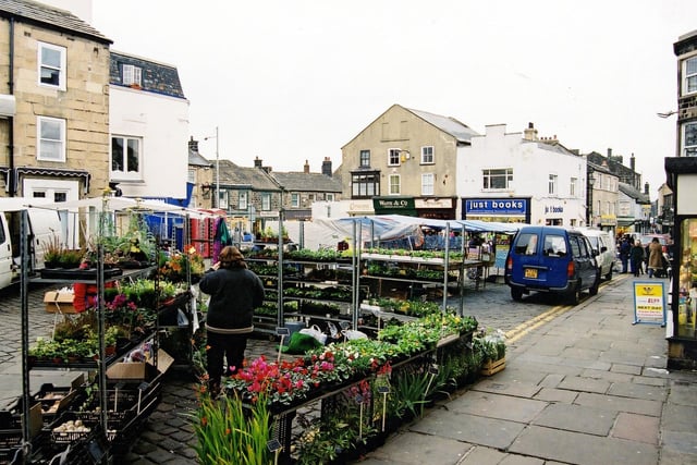 Otley Market Place in October 2003. Otley has boasted a market since a charter was granted by Henry III in 1222. A further Royal Charter in 1248 enabled Otley to hold a regular Monday market but it was not until 1800 that the market was moved to this location. There were no shops here at the time, only old timber shambles. Nowadays, the thriving market attracts many visitors to the town and is held weekly on Tuesdays, Fridays and Saturdays. A wide range of goods and produce is available including the colourful array of plants displayed on this stall.
