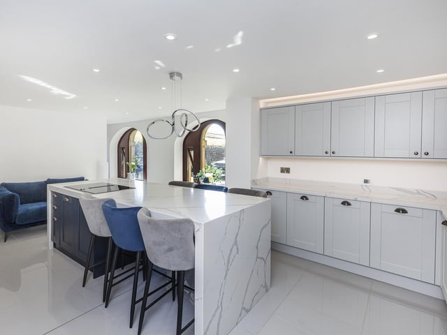 A sleek and shiny breakfast kitchen has shaker style units and Quartz work tops, an island with breakfast bar, and integrated appliances