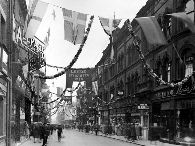 A view looks down Upperhead Row which has been decorated for Civic Week celebrations. On the left are the premises of Allpass and Co.,Home Furnishers. On the right is Everleigh Bishop, jewellers, then Louis McKennell, tailors. Flags, garlands and bunting hang across the street.