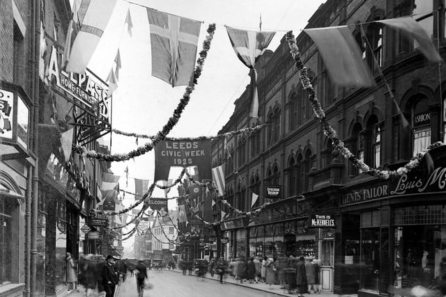 A view looks down Upperhead Row which has been decorated for Civic Week celebrations. On the left are the premises of Allpass and Co.,Home Furnishers. On the right is Everleigh Bishop, jewellers, then Louis McKennell, tailors. Flags, garlands and bunting hang across the street.