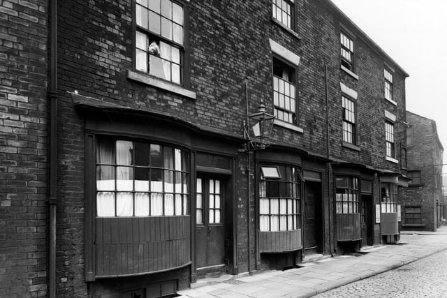 South-east side view Water Lane, known as Crofts buildings. Three storey brick buildings with bowed wooden windows on ground floor. Street lights on wall. Child looking out of second floor window. Man and woman looking out of corner on ground floor. Pictured in  August 1950.