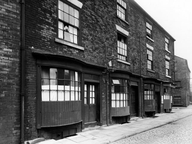 South-east side view Water Lane, known as Crofts buildings. Three storey brick buildings with bowed wooden windows on ground floor. Street lights on wall. Child looking out of second floor window. Man and woman looking out of corner on ground floor. Pictured in August 1950.