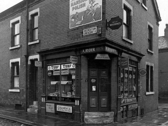 Recreation Crescent in January 1954. Picture shows the premises of A. Ryder, confectionery shop. Recreation Row is visible on the right. Advertisements for Lyons cakes, Turf cigarettes, Brooke Bond tea, St. Bruno Flake tobacco, Robin cigarettes are all visible outside the shop. A billboard advertises Mansion Polish.