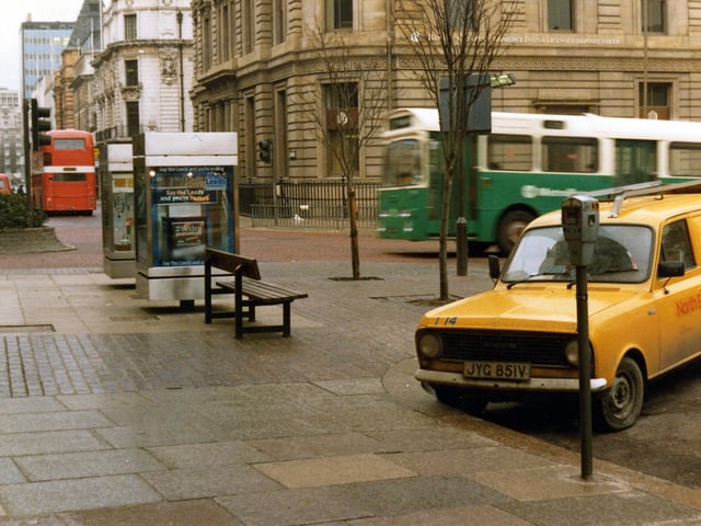 The Headrow seen from the junction with Cookridge Street. Park Row is on the left. Two advertising display boxes can be seen in the centre. A van is parked in the foreground and two buses are visible. Pictured in November 1980.