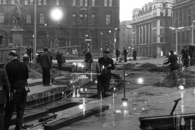 Workers most likely dismantling disused tram track in City Square at a time when the Square was undergoing alterations. The photograph was taken in early evening or morning judging by the light. Either part of another, earlier, image can be seen superimposed in the centre with a glimpse of a tram, destination Corn Exchange, or the image was taken through the window of a bus, producing the same effect. Pictured in July 1956.