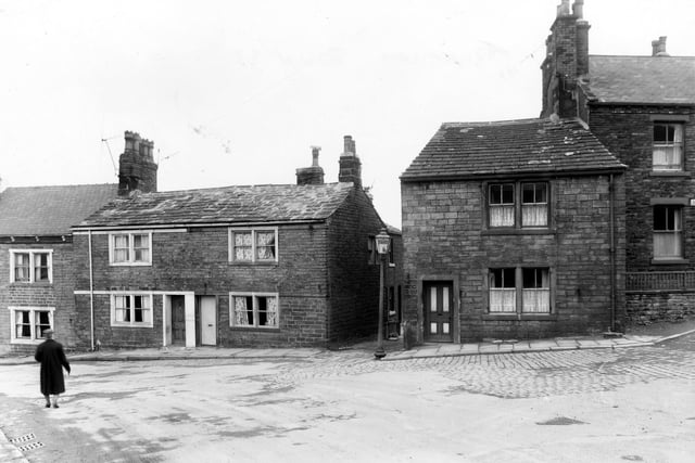 A view of the junction of Bellmount Grove. A woman can be seen walking along Bell Lane on the left. The stone cottages are from the left, numbers 78, 76 and 74 Bell Lane. A gas street lamp stands at the entrance to Daisy Hill outside number 72 Bell Lane. On the far right number 1 Bellmount Grove can be partially seen.