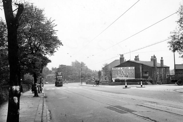 Looking south east down Harrogate Road towards the junction with Harehills Lane and Chapeltown Road in September 1951. Potternewton Lane turns off on the right. A sign advertises 'Lewis's Department Store'. On the left a tram can be seen approaching a zebra crossing. People wait at a tram stop.