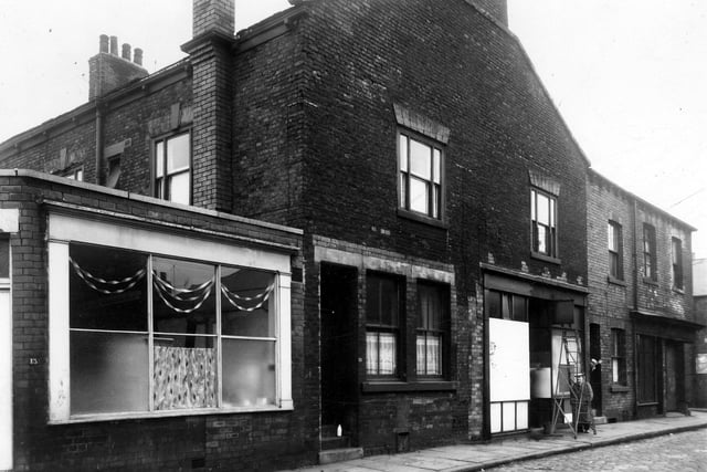 Leek Street in December 1960 On the left is number 13 with Christmas streamers hanging in the window. On the right is number 15 where a milk bottle awaits collection from the doorstep. A man in overalls stands by a ladder outside number 17b which appears to be undergoing exterior decoration while on the right someone peers out from the doorway of number 17a. At the end of the row is number 17, here is Endon Street.