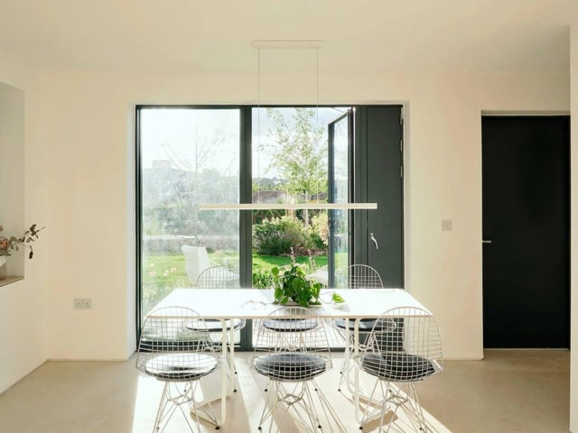 Flanked by a wide glazed screen that opens to a patio, the dining area flows seamlessly into a centrally positioned kitchen with sleek bespoke cabinetry and a generous breakfast bar.